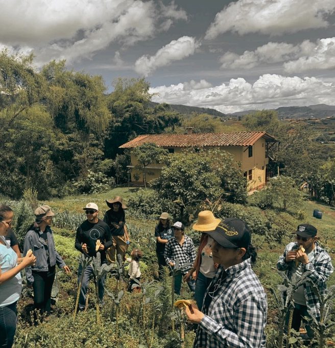 Familias recorriendo la huerta de Kundina, con la casa de la finca y las montañas al fondo
